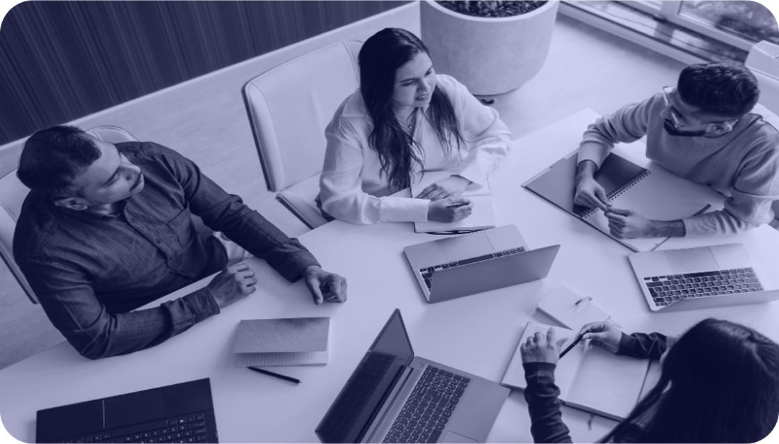 Equipo de trabajo en reunión con laptops y cuadernos sobre la mesa